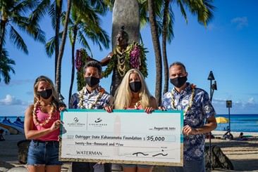 Two women and two men wearing face masks on the beach hold a large check