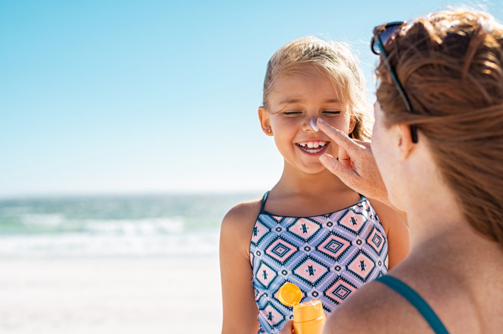 mother applying sunscreen to little girl