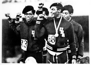 Photo of Olympians Ron Freeman, Lee Evans, Larry James, and Vincent Matthews in black berets holding up fists.