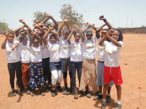 Group of Guinean girls wearing shoes and holding up their arms.